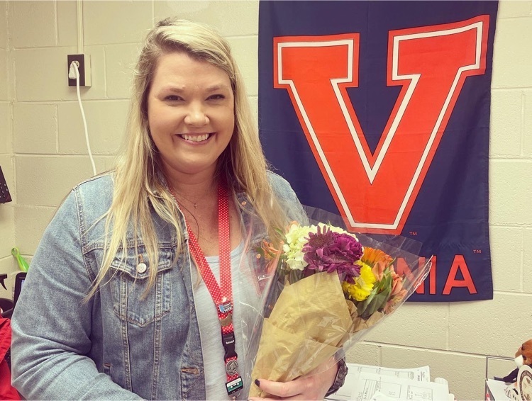 Teacher of the Year, Mrs. Powell, holds a bouquet of flowers in front of a UVA flag  